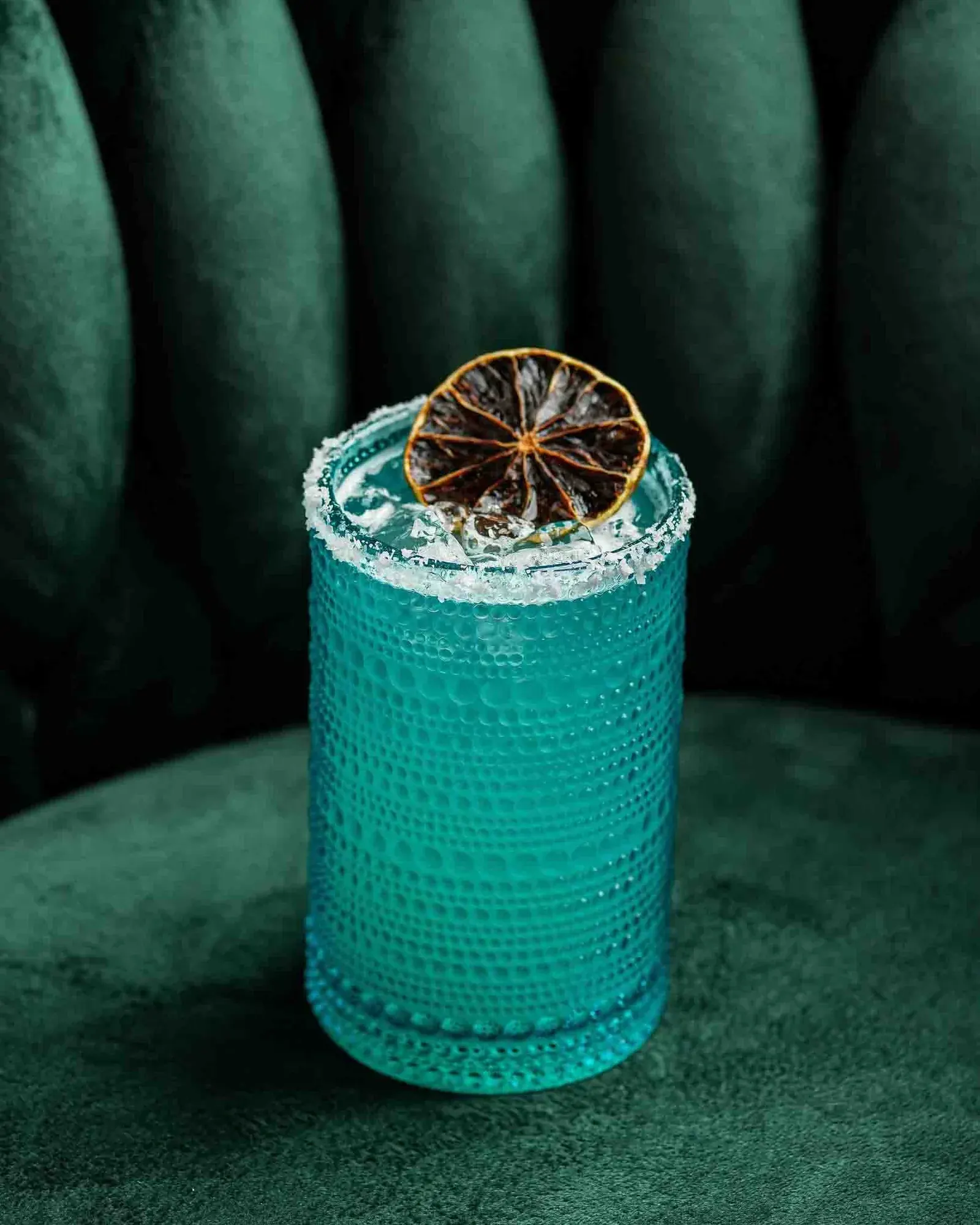 A turquoise cocktail with a dried citrus wheel