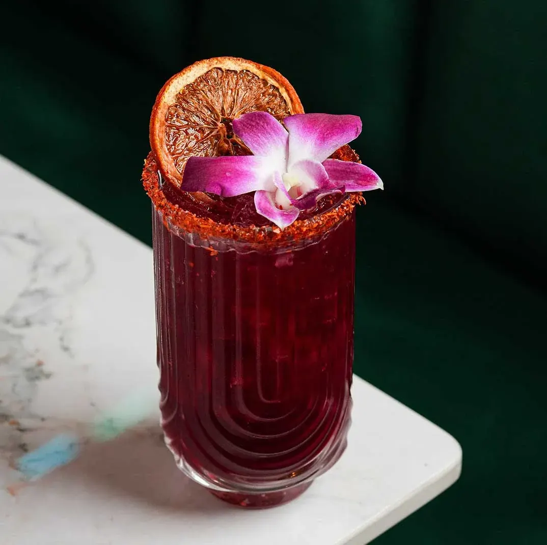A deep red cocktail with an orchid